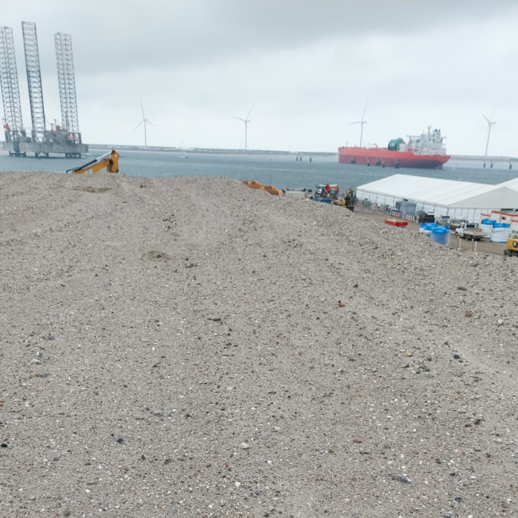 Opgeslagen partij grond op een haventerrein met kranen op de achtergrond