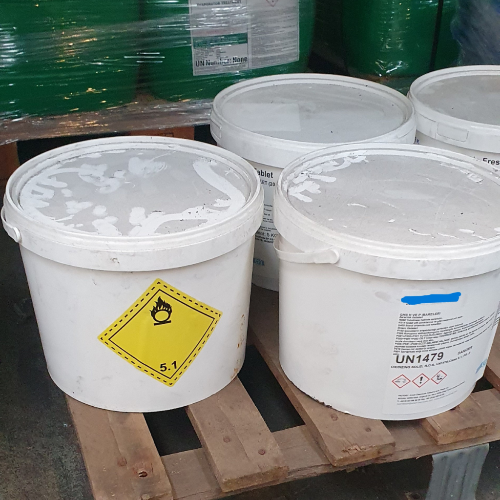 Witte vaten met gevaarlijke stoffen op een pallet, voorzien van gevaarsetiket