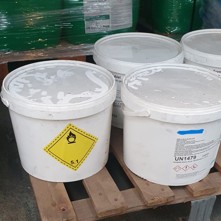 Witte vaten met gevaarlijke stoffen op een pallet, voorzien van gevaarsetiket