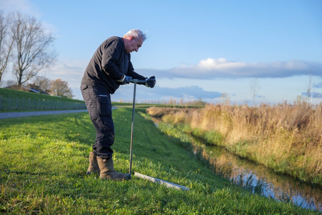 Veldwerker meet langs een sloot in een weiland