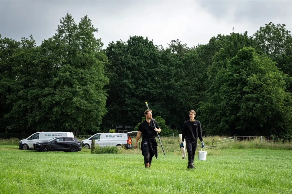 Medewerkers van Buro Antares op weg naar een onderzoekslocatie, bedrijfsbusjes op de achtergrond